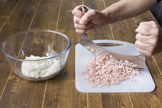 Tritate finemente il prosciutto cotto aiutandovi con una mezzaluna, quindi unitelo ad una parte del composto di formaggio e yogurt, amalgamandolo per bene. 