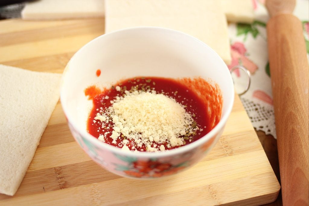 In una ciotola uniamo qualche cucchiaio di salsa di pomodoro con origano, sale e il formaggio grattugiato. 