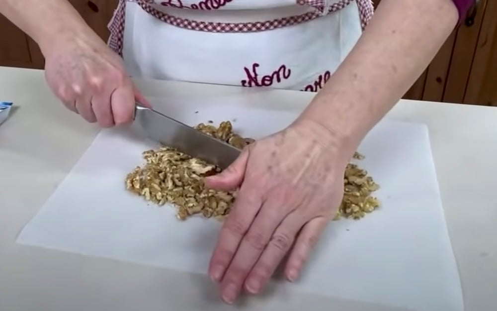 Per prima cosa tritiamo grossolanamente i gherigli di noci utilizzando tagliere (o un pezzo di carta forno) e coltello.
