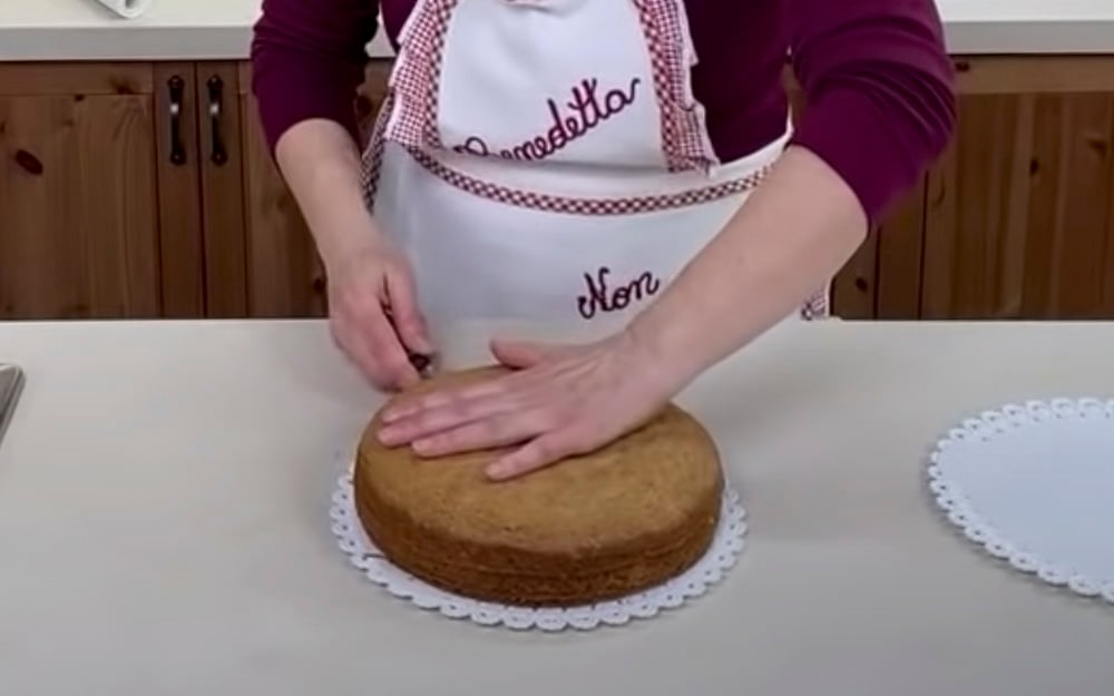 Una volta cotta, sforniamo la torta e passiamo alla farcitura: rovesciamola su un sottotorta per staccare il fondo della teglia e la carta forno. Rigiriamola e con un coltello seghettato la tagliamo a metà.