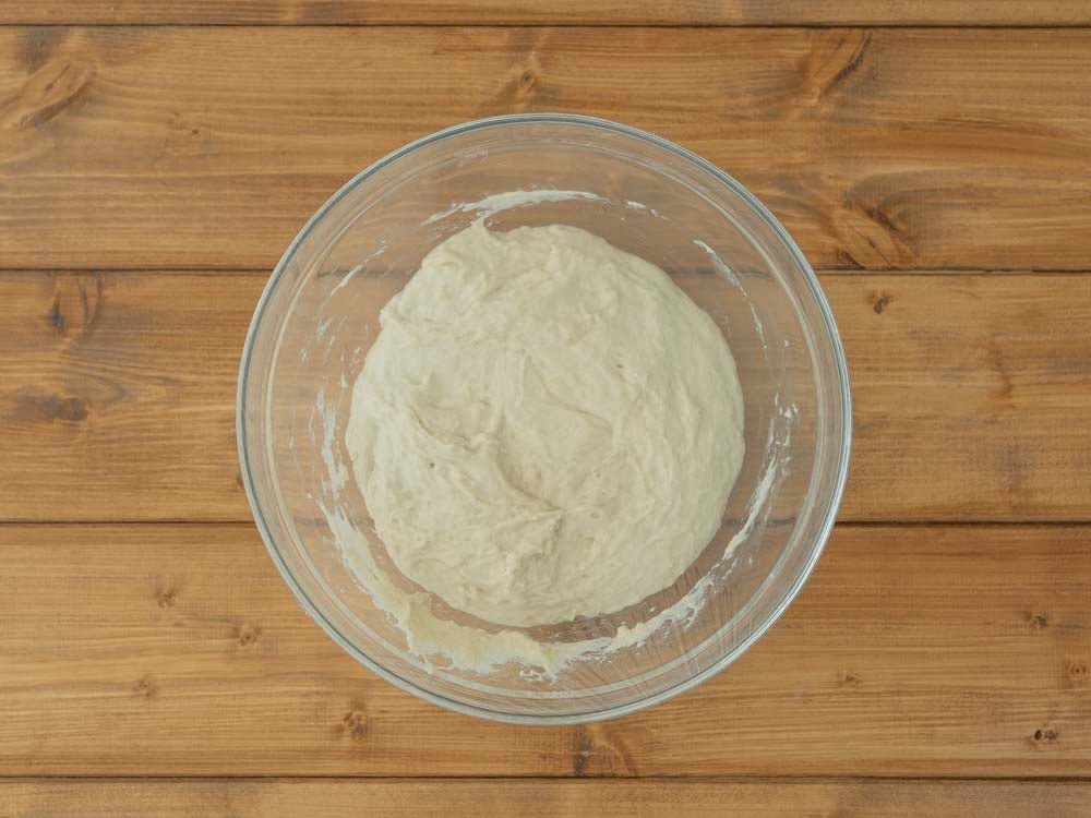Quando abbiamo usato metà della farina, aggiungiamo un cucchiaino di sale e continuiamo a mescolare. Al termine l'impasto risulterà molto denso e appiccicoso. Copriamo con la pellicola e lasciamo lievitare in luogo caldo fino al raddoppio del volume. Ci vorranno circa 2 ore. 