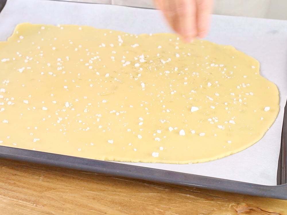 Trasferiamo la carta forno con l’impasto steso sulla placca del forno, aggiungiamo sulla superficie un po’ di sale grosso e un po’ di rosmarino (secco o fresco a piacere).