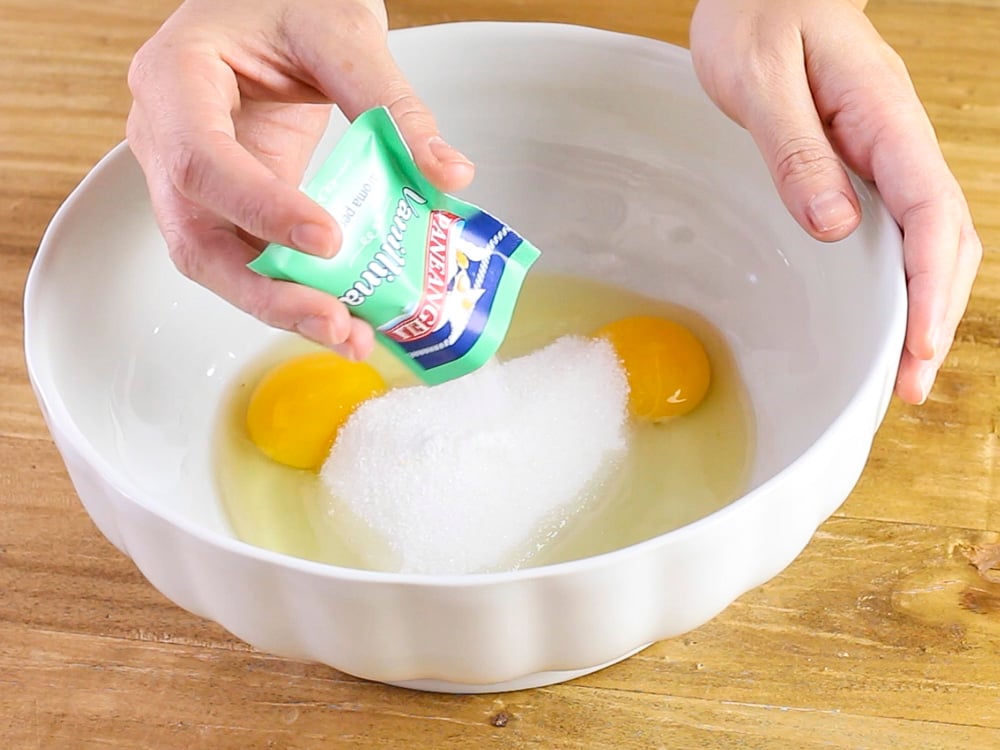 In una ciotola rompiamo le uova, aggiungiamo lo zucchero, la bustina di vanillina e mescoliamo con una frusta.