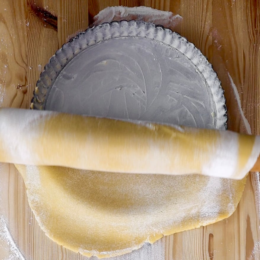 Avvolgiamo la pasta nel mattarello e dopo aver imburrato e infarinato uno stampo per crostata da 24 cm di diametro, sistemiamo l’impasto nella tortiera eliminando i bordi in eccesso.